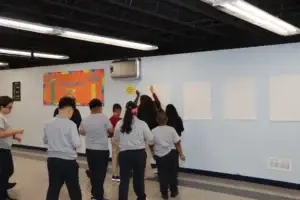 Students place their written sticky notes on display sheets along the cafeteria wall.