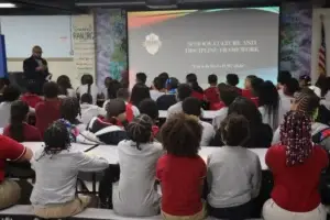 A staff member speaks to students seated in front of the School Culture and Discipline Framework presentation.